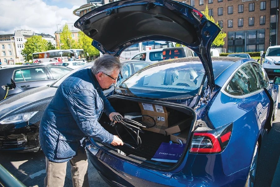A man placing a charging cable in his car at an electric car parking lot in Oslo, Norway.