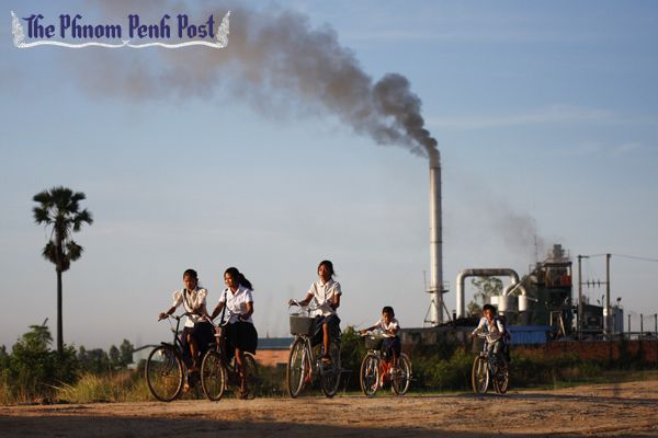Children ride past a factory on their way home from school on the outskirts of Phnom Penh as its chimney spews out emissions. Heng Chivoan