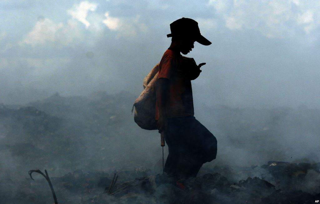 Smoke from burning trash fires swirls around a Cambodian boy as he scavenges a dump on the outskirts of Phnom Penh, file photo.